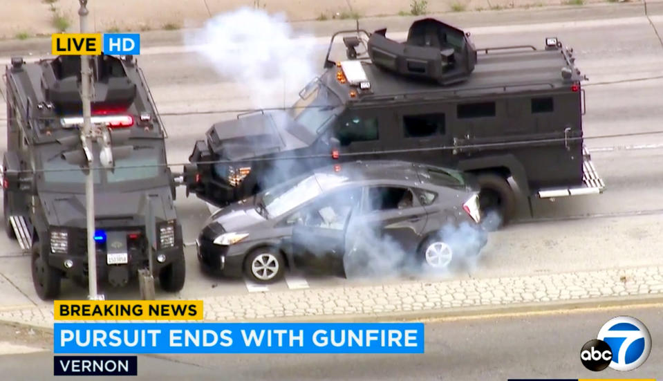 In this photo taken from video provided by KABC-TV, armored police vehicles block a car and deploy a flash bang device at the conclusion of a wild car chase and shootout in the Los Angeles area Friday afternoon, May 10, 2019. The car finally came to a halt in the Los Angeles suburb of Vernon, where the bloodied woman driver surrendered. The gunman remained in the car. The man, who appeared to be wounded, was removed from the car and taken to a hospital. His condition was not immediately known. (KABC-TV via AP)