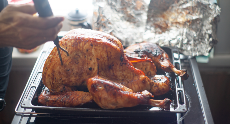 person's hand putting thermometer in large turkey on baking sheet 