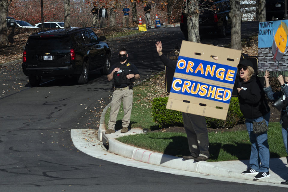 In this image made through the window of the press vehicle accompanying the motorcade carrying President Donald Trump, people hold signs at the entrance of Trump National Golf Club, Sunday, Nov. 8, 2020, in Sterling, Va. (AP Photo/Evan Vucci)