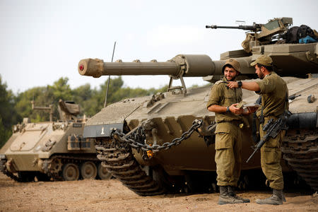 Israeli soldiers speak next to a tank as military armoured vehicles gather in an open area near Israel's border with the Gaza Strip October 18, 2018. REUTERS/Amir Cohen