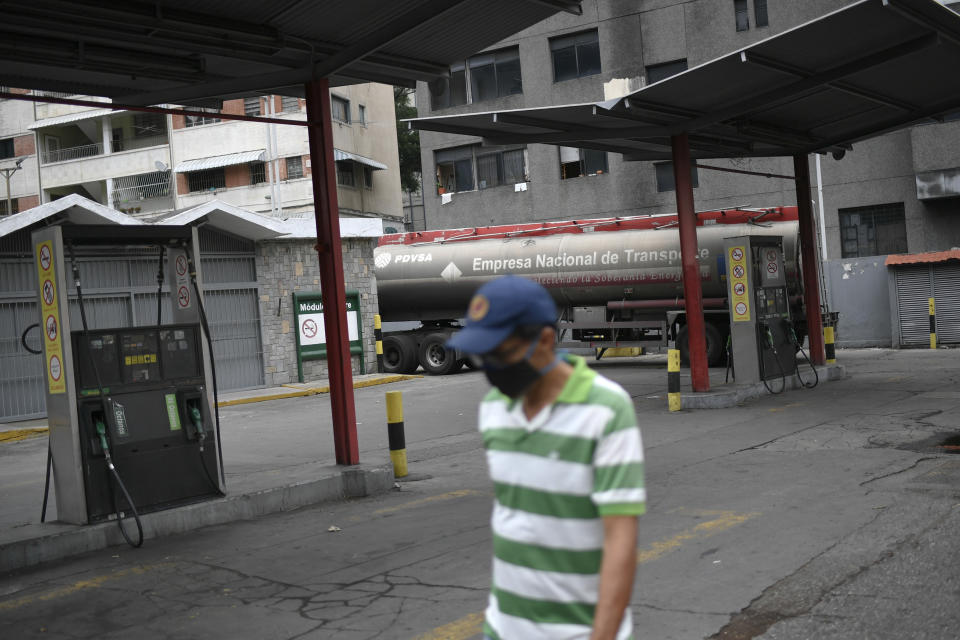 Un hombre con cubrebocas para protegerse del contagio del nuevo coronavirus camina frente a una estación de servicio de una compañía petrolera estatal vacía mientras un camión cisterna descarga gasolina en Caracas, Venezuela, el domingo 31 de mayo de 2020. (Foto AP/Matías Delacroix)