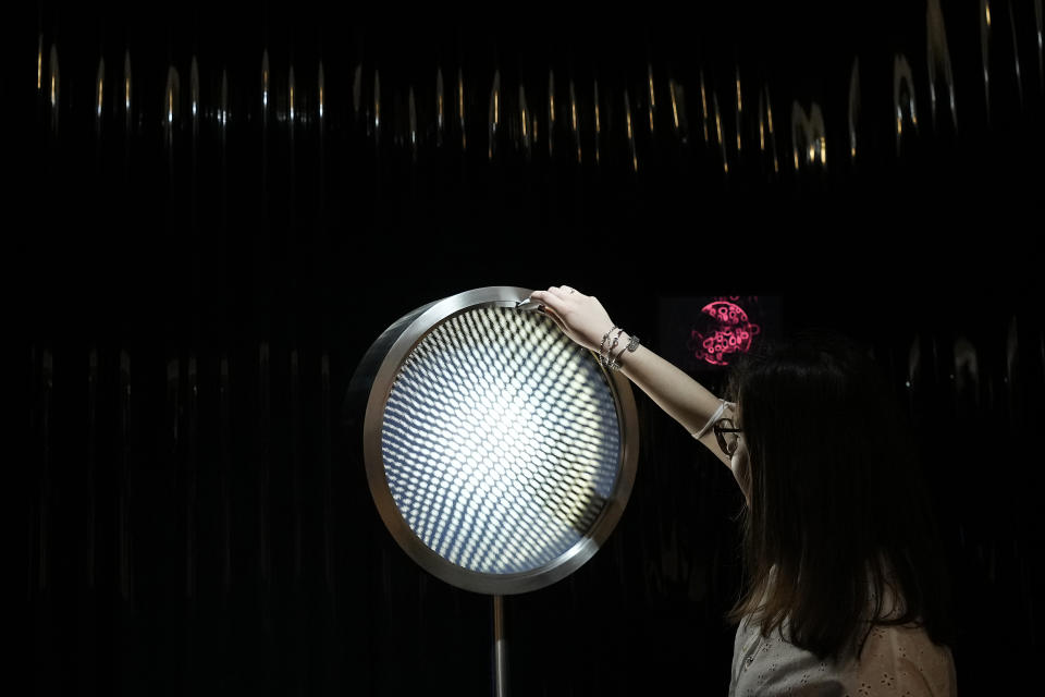 A woman touches a creation by Alessi's furniture designers, part of the Design Fair exhibition in Milan, Italy, Wednesday, June 8, 2022. (AP Photo/Antonio Calanni)