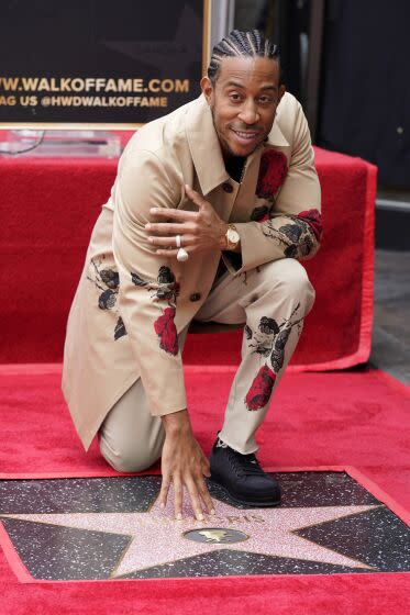 Ludacris, wearing a tan coat and pants, poses with hand resting on his star on the Hollywood Walk of Fame.