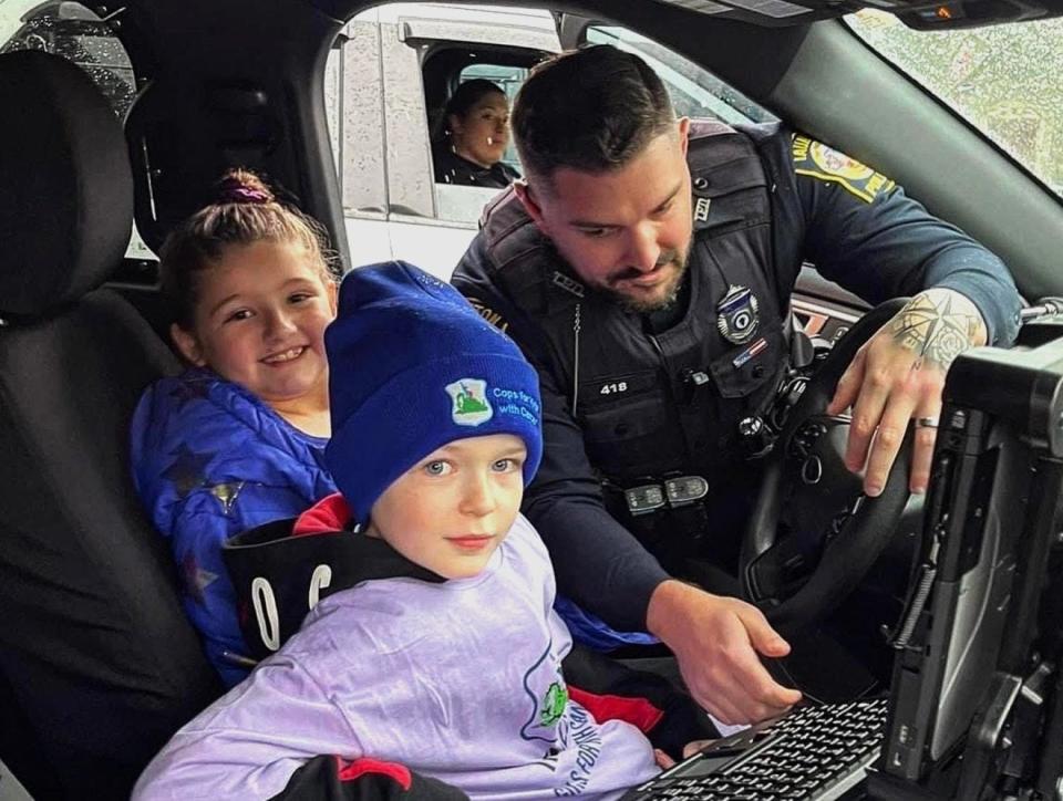 From left, Alexis Dupra, Jace Dupra and Taunton Police Officer Evan Lavigne as Lavigne shows them his cruiser. Jace, who is battling stage four medulloblastoma, stopped by the station with his family to receive a donation from Cops for Kids with Cancer on Monday, Jan. 16, 2023.