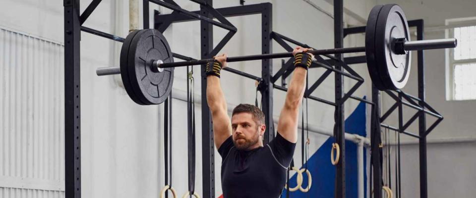 Muscular man training lunges with barbells over head