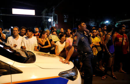 A police officer stands next to residents as they watch the body of a man (not pictured), who police said was killed in a spate of drug related violence overnight in Manila, Philippines August 16, 2017. REUTERS/Dondi Tawatao