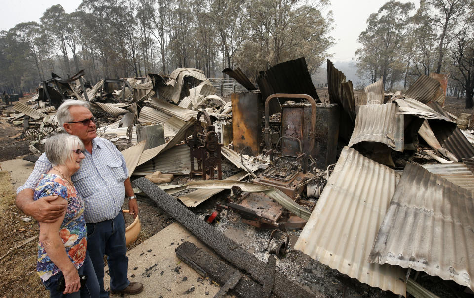 A man and woman stand looking at their burnt down property.