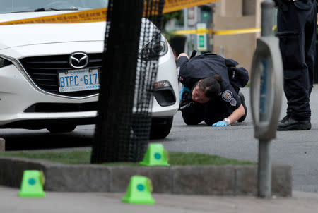 FILE PHOTO: A police officer looks for evidence under a car while investigating a mass shooting on Danforth Avenue in Toronto, Ontario, Canada, July 23, 2018. REUTERS/Chris Helgren/File Photo