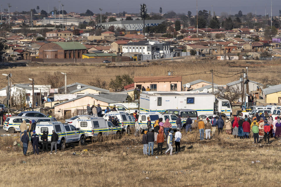 People gather at the scene of an overnight bar shooting in Soweto, South Africa, Sunday July 10, 2022. A mass shooting at a tavern in Johannesburg's Soweto township has killed 15 people and left others in critical condition, according to police. Police say they are investigating reports that a group of men arrived in a minibus taxi and opened fire on some of the patrons at the bar shortly after midnight Sunday. (AP Photo/Shiraaz Mohamed)