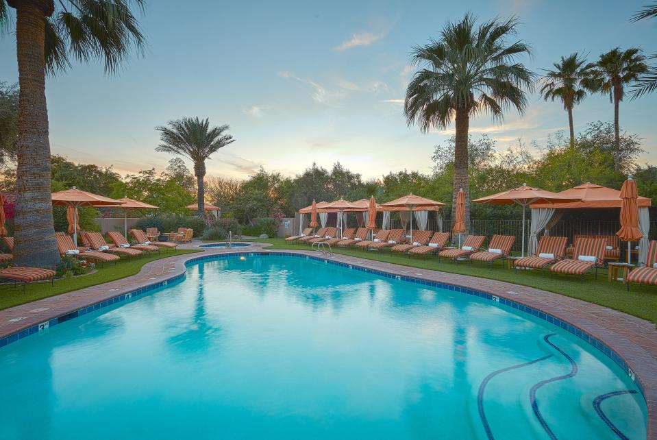 An empty pool surrounded by empty orange beach chairs and umbrellas