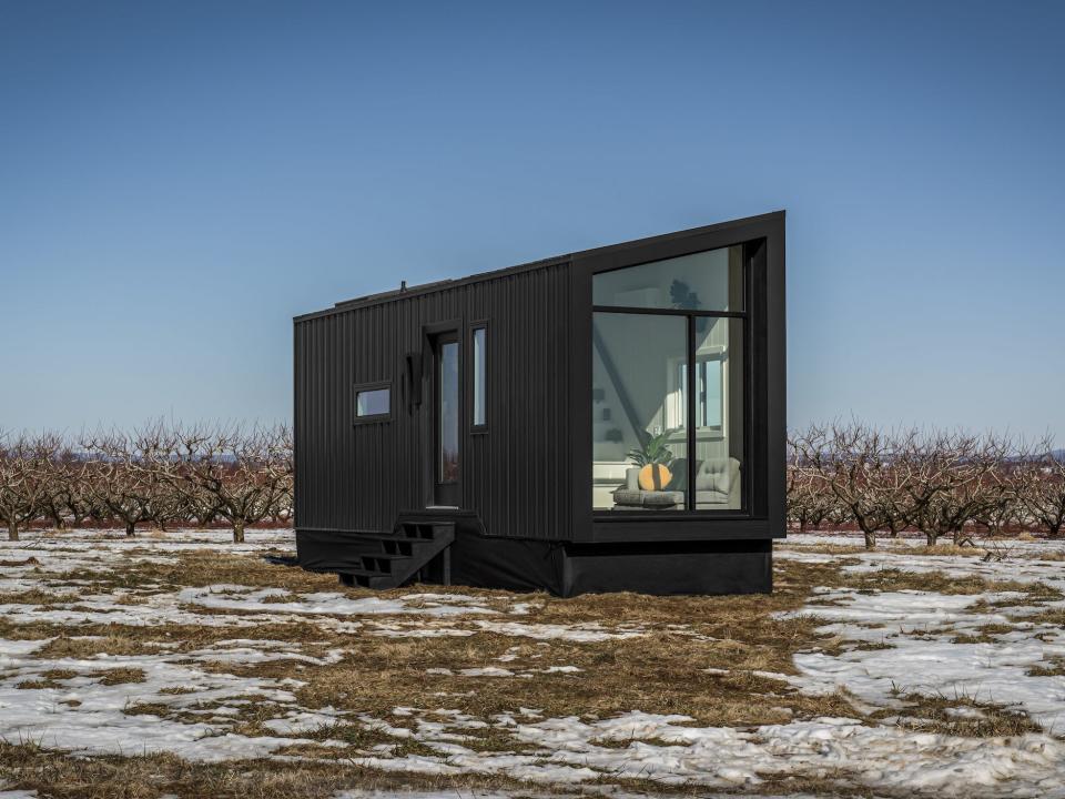 a black tiny home with a large glass wall on a snowy field at sunset