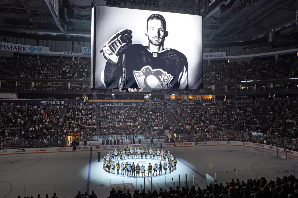 The Pittsburgh Penguins and Anaheim Ducks gather at center ice, before an NHL hockey game in Pittsburgh, Monday, Oct. 30, 2023, to honor former Penguin player Adam Johnson, shown on scoreboard, who died in while playing in an English hockey league game. (AP Photo/Gene J. Puskar)