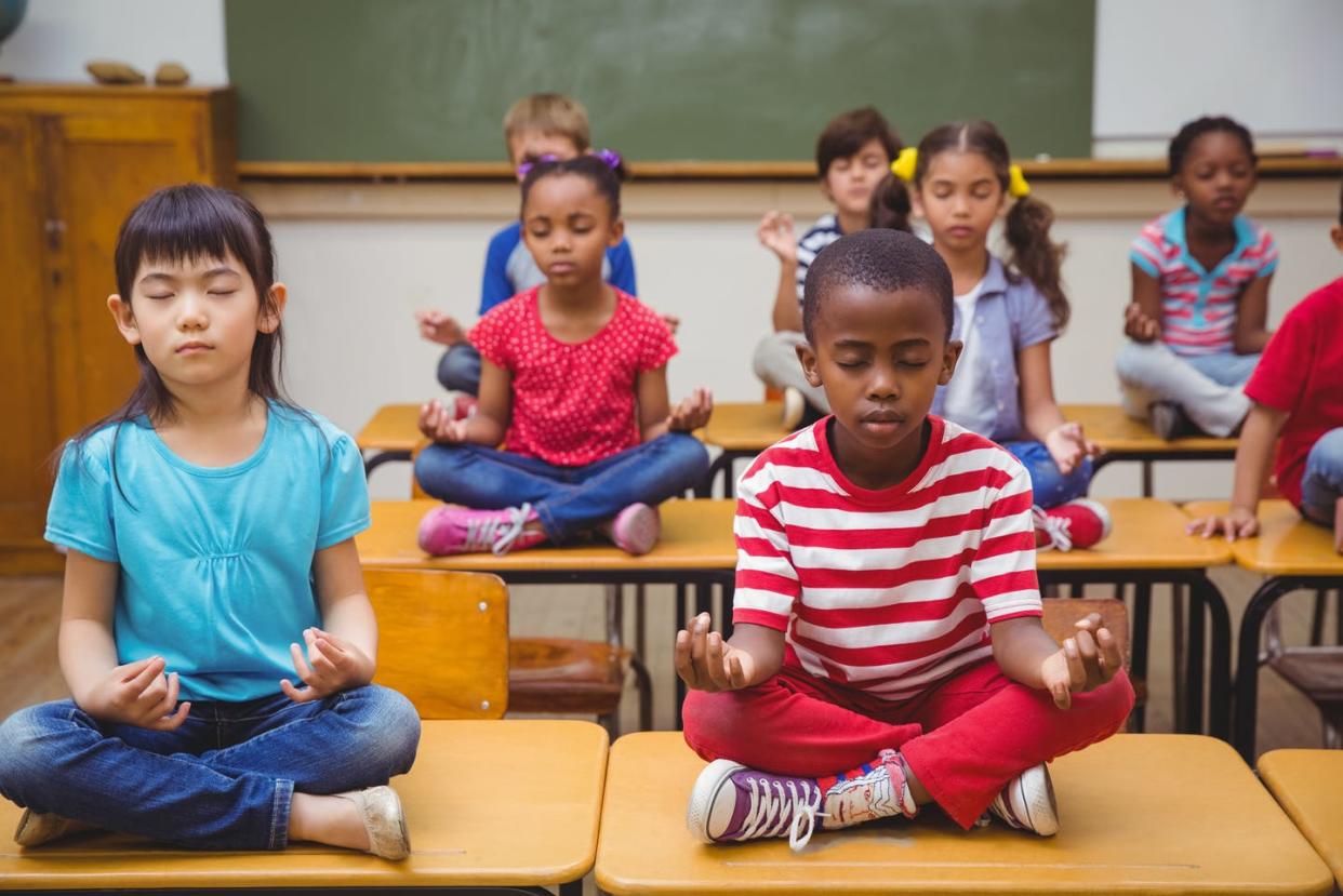 <span class="caption">For both children and adults, practicing mindfulness can improve brain function and enhance the immune system.</span> <span class="attribution"><a class="link " href="https://www.gettyimages.com/detail/photo/pupils-meditating-in-lotus-position-on-desk-royalty-free-image/469970618?adppopup=true" rel="nofollow noopener" target="_blank" data-ylk="slk:Wavebreakmedia via Getty Images;elm:context_link;itc:0;sec:content-canvas">Wavebreakmedia via Getty Images</a></span>