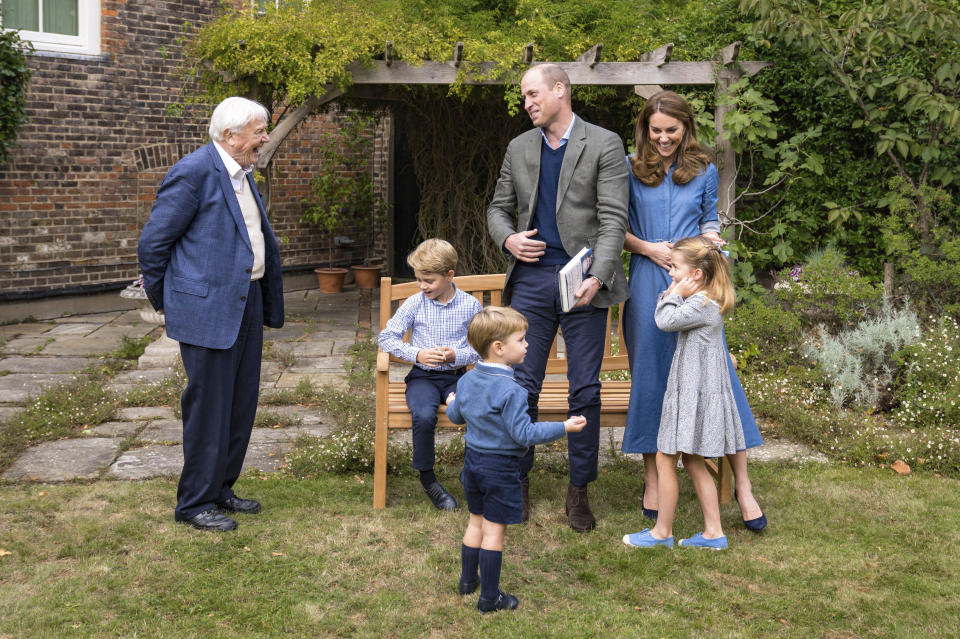 In this Thursday, Sept. 24, 2020 photo released by Kensington Palace, Britain's Prince William, centre, and Kate, the Duchess of Cambridge, react with Naturalist David Attenborough, left, with their children, Prince George, seated, Princess Charlotte, right and Prince Louis, foreground, in the gardens of Kensington Palace in London after Prince William joined Attenborough to watch a private outdoor screening of his upcoming film - David Attenborough: A Life On Our Planet. (Kensington Palace via AP)