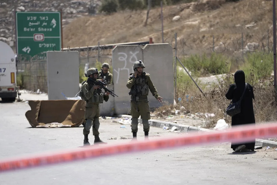 Israeli soldiers speak to a Palestinian woman near the site of an alleged car-ramming attack near Beit Hagai, a Jewish settlement in the hills south of the large Palestinian city of Hebron, Wednesday, Aug. 30, 2023. The Israeli military said security forces shot the Palestinian driver as he accelerated toward a military post. A soldier struck by the car was evacuated to a nearby hospital for treatment. There was no immediate word on the condition of the suspected Palestinian assailant. (AP Photo/Mahmoud Illean)