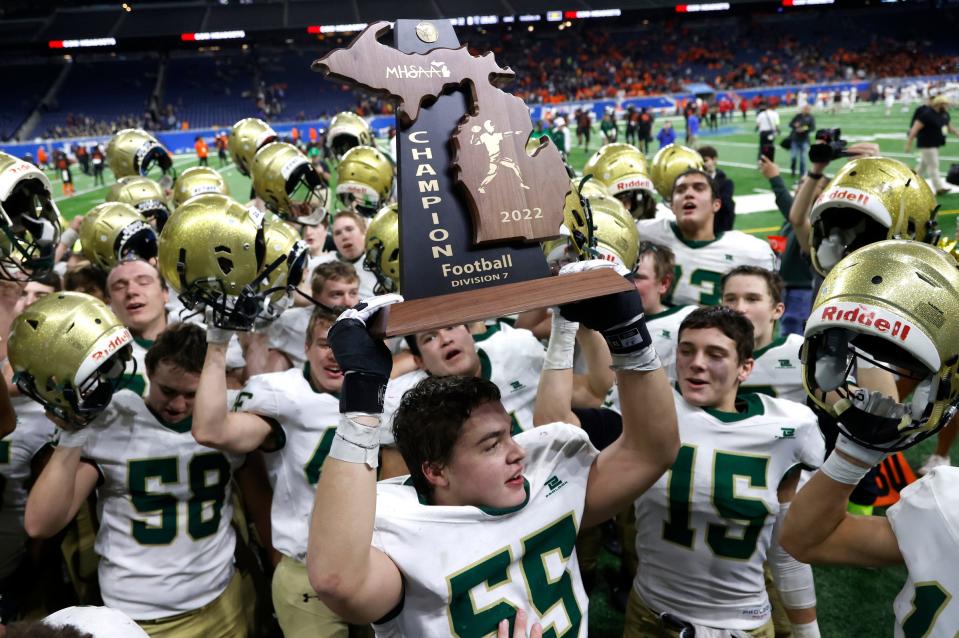 Jackson Lumen Christi's Cooper Cumberworth holds the 2022 MHSAA Division 7 high school football trophy as he and his teammates sing their school fight song after defeating Traverse City St. Francis, 15-12, in the state finals at Ford Field in Detroit on Nov 26, 2022.