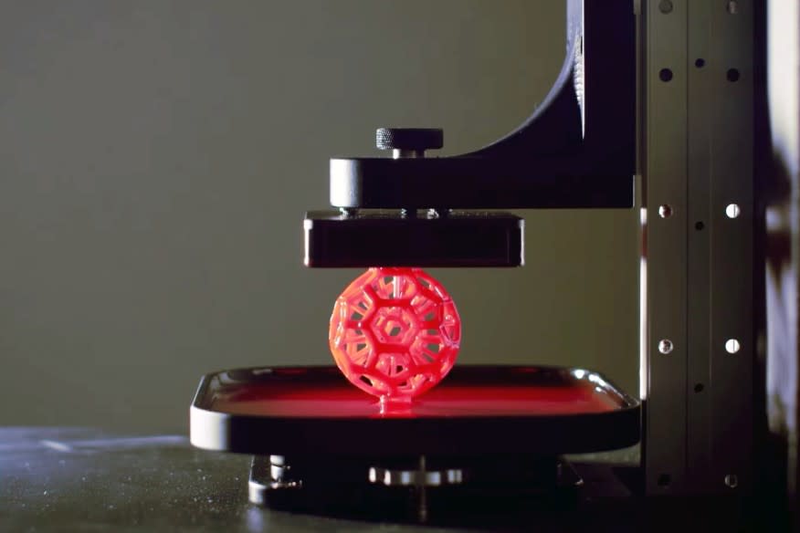 A red lattice-like ball rising from a pool of liquid as it's printed using Carbon's 3D printing tech.