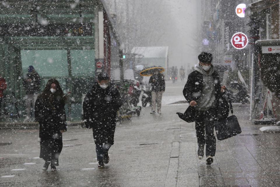 Pedestrians wearing face masks to help protect against the spread of the coronavirus move through the falling snow in Seoul, South Korea, Thursday, Jan. 28, 2021. (AP Photo/Ahn Young-joon)
