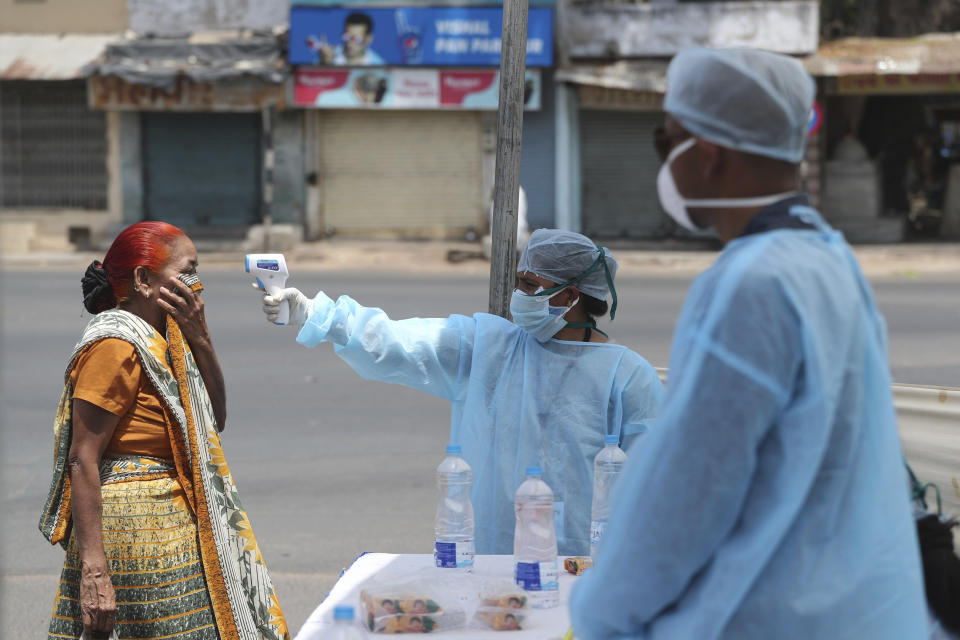 FILE-In this April 8, 2020 file photo, an Indian health worker checks the temperature of a woman during lockdown to prevent the spread of new coronavirus in Ahmedabad, India. India, a bustling country of 1.3 billion people, has slowed to an uncharacteristic crawl, transforming ordinary scenes of daily life into a surreal landscape. The country is now under what has been described as the world’s biggest lockdown, aimed at keeping the coronavirus from spreading and overwhelming the country’s enfeebled health care system. (AP Photo/Ajit Solanki, File)