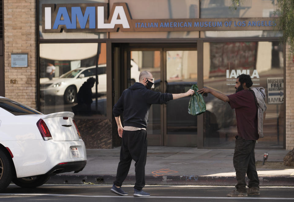 A driver steps out of his vehicle to offer a bag with prepared food to a homeless person in downtown Los Angeles Thursday, Nov. 26, 2020. Americans are marking the Thanksgiving holiday Thursday amid an unrelenting pandemic that has claimed the lives of more than a quarter of a million people in the United States. (AP Photo/Damian Dovarganes)