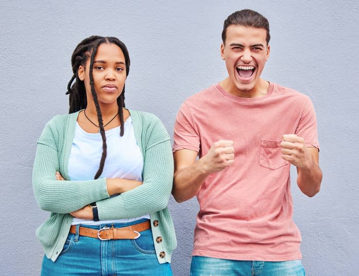 Two people standing side by side one appears frustrated the other overly excited