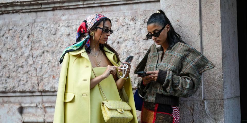 milan, italy september 21 melanie darmon r wears a gold hair clip, black sunglasses, gold earrings, a brown with blue and red checkered print pattern oversized jacket, a red black white embroidered wool pattern knees skirt, gabriella berdugo l wears a red blue white print pattern silk scarf on the head, black sunglasses, silver earrings, gold necklaces, a yellow shoulder off short dress, a pale yellow jacket, a pale yellow and white tweed crossbody bag from chanel, outside alberta ferretti, during the milan fashion week womenswear springsummer 2023 on september 21, 2022 in milan, italy photo by edward berthelotgetty images