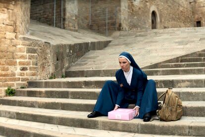 Betty Gilpin as Simone sits on steps holding a pink box in Mrs. Davis