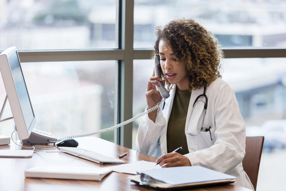 Doctor in white coat talking on phone at their desk w