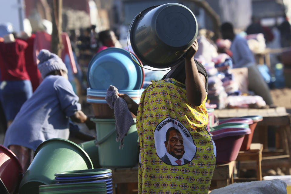 A woman inspects a bucket while wearing a cloth with a portrait of Zimbabwean President Emmerson Mnangagwa in Harare, Thursday, Aug, 8, 2019. Many Zimbabweans who cheered the downfall of longtime leader Robert Mugabe two years ago now find the country's economy worse than before.(AP Photo/Tsvangirayi Mukwazhi)