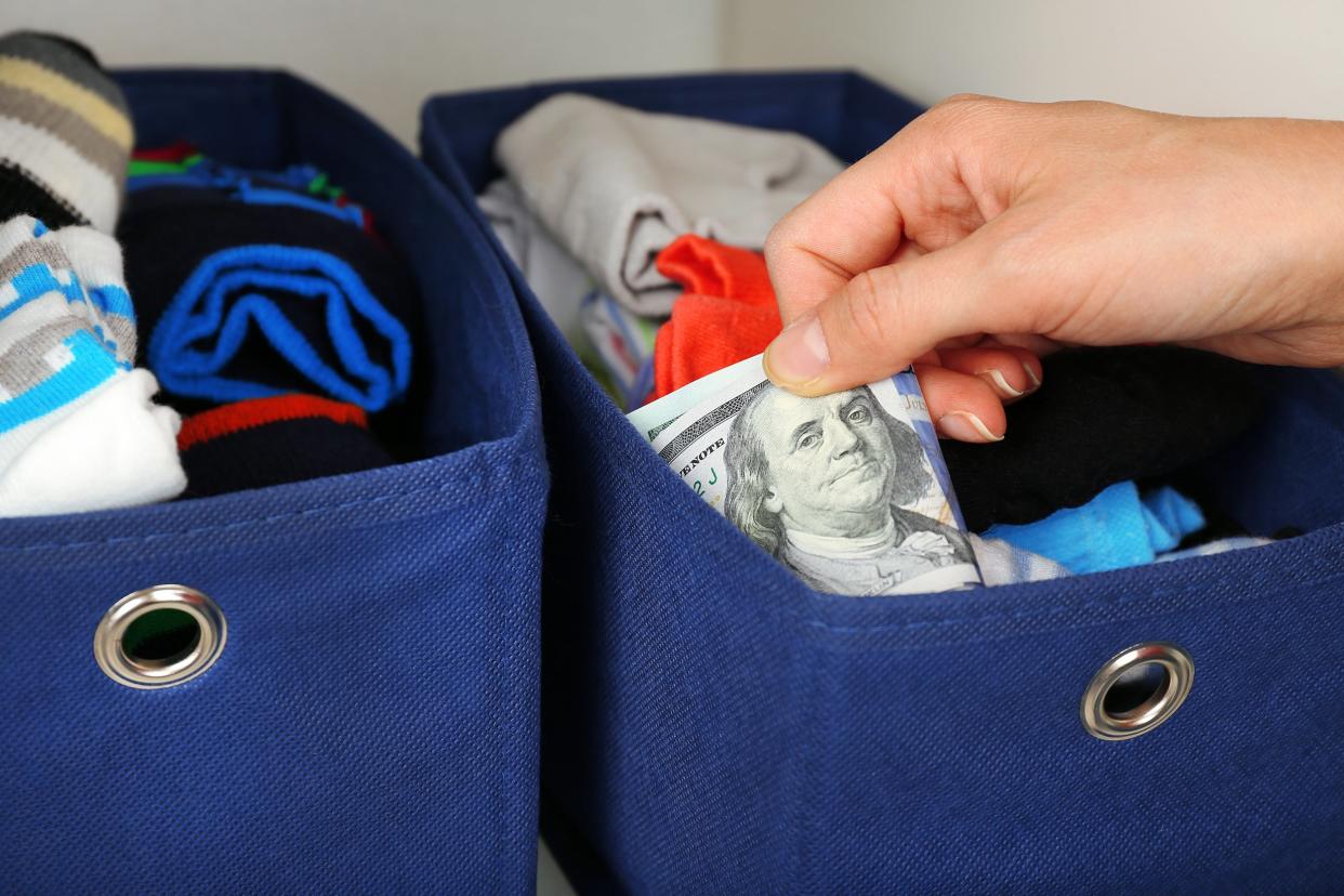 Closeup of hand hiding money in a box of clothes