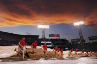 Grounds crew workers run with the tarp as the sun sets after a rain delay during the third inning of a baseball game between the Cleveland Guardians and the Boston Red Sox at Fenway Park, Monday, July 25, 2022, in Boston. (AP Photo/Charles Krupa)