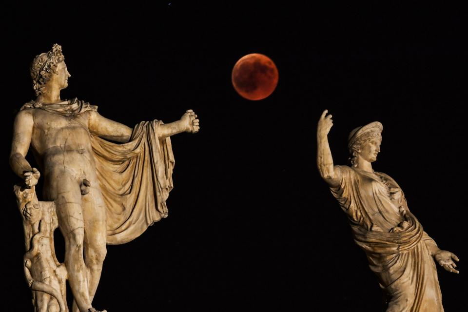 <p>A picture shows the full moon during a “blood moon” eclipse beside a statue of ancient Greek goddess Hera (R) and god Apollo in central Athens on July 27, 2018. (Photo: Aris Messinis/AFP/Getty Images) </p>