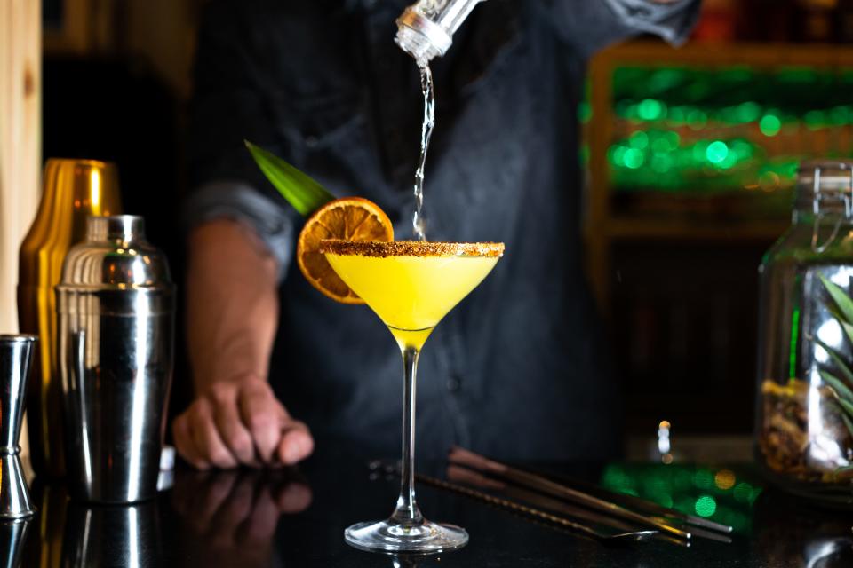 Bartender pouring alcohol on a cocktail in a night club bar.