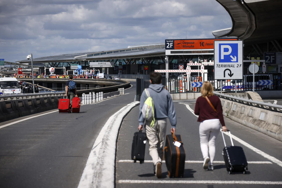 Travelers arrive on foot at Roissy-Charles de Gaulle airport while airport workers demonstrate, Friday, July 1, 2022 at Roissy airport, north of Paris. Flights from Roissy-Charles de Gaulle airport in Paris and other French airports faced disruptions Friday as airport workers held a strike and protests to demand salary hikes to keep up with inflation. It's the latest trouble to hit global airports this summer, as travel resurges after two years of virus restrictions. (AP Photo/ Thomas Padilla)