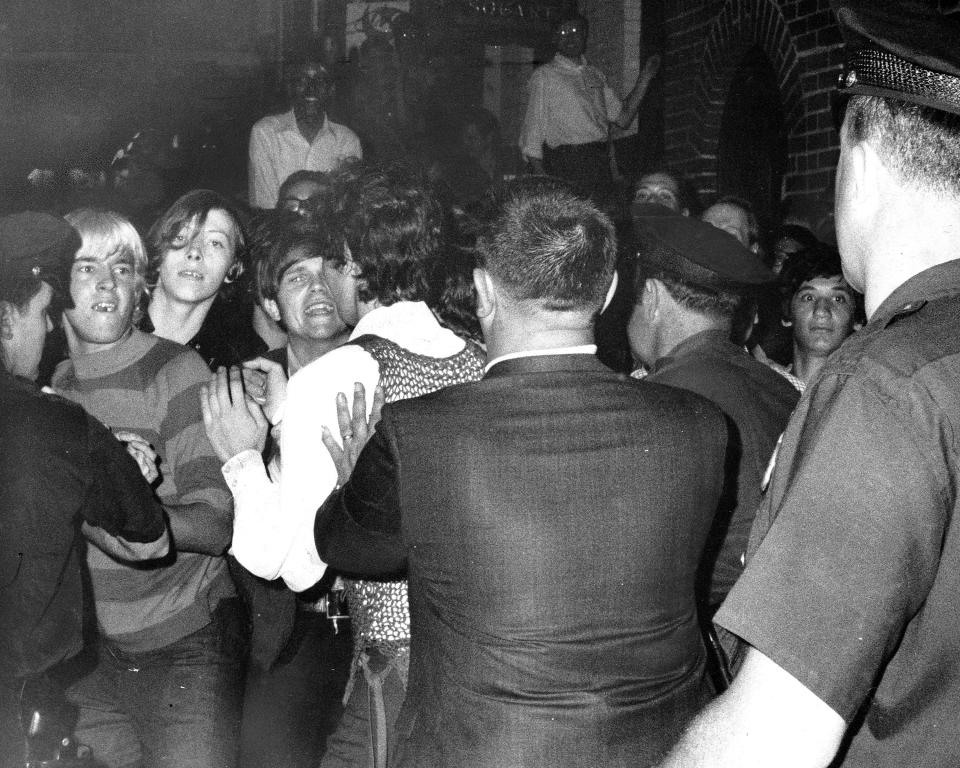 A black and white photo of police in front of an angry crowd in front of a bar.