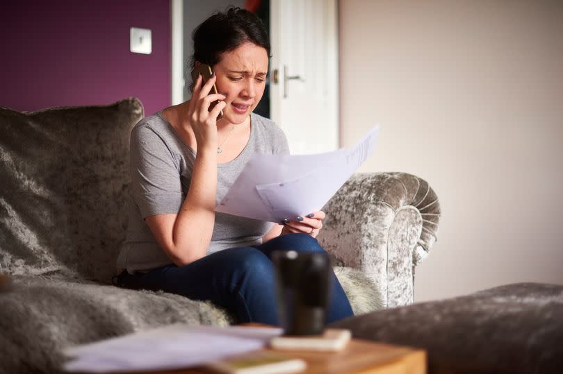 A young woman sat on the sofa talking on the phone while holding paperwork