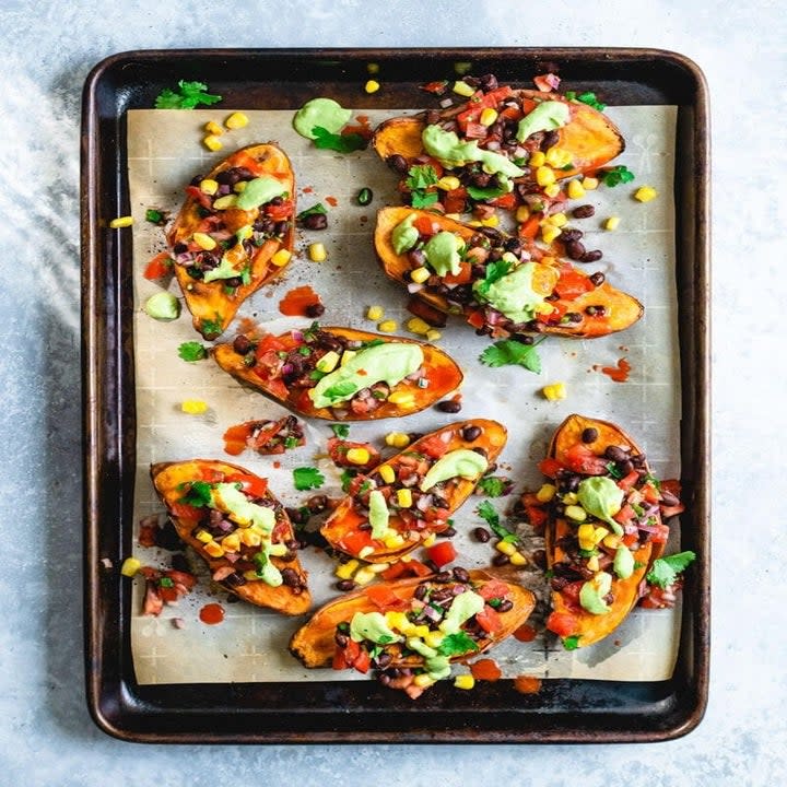 A tray with sweet potatoes halved with avocado, beans, corn, and peppers on it