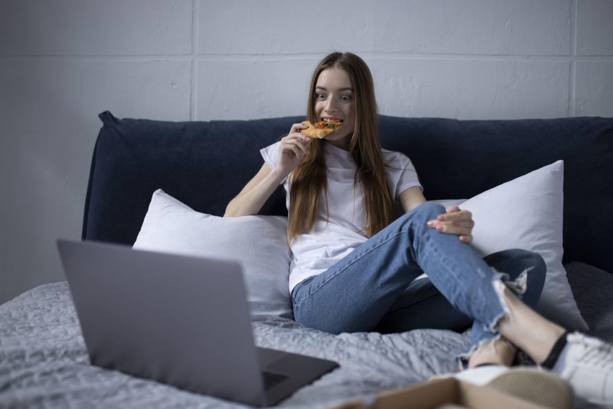 Happy young woman eating slice of hot pizza at home and watching tv