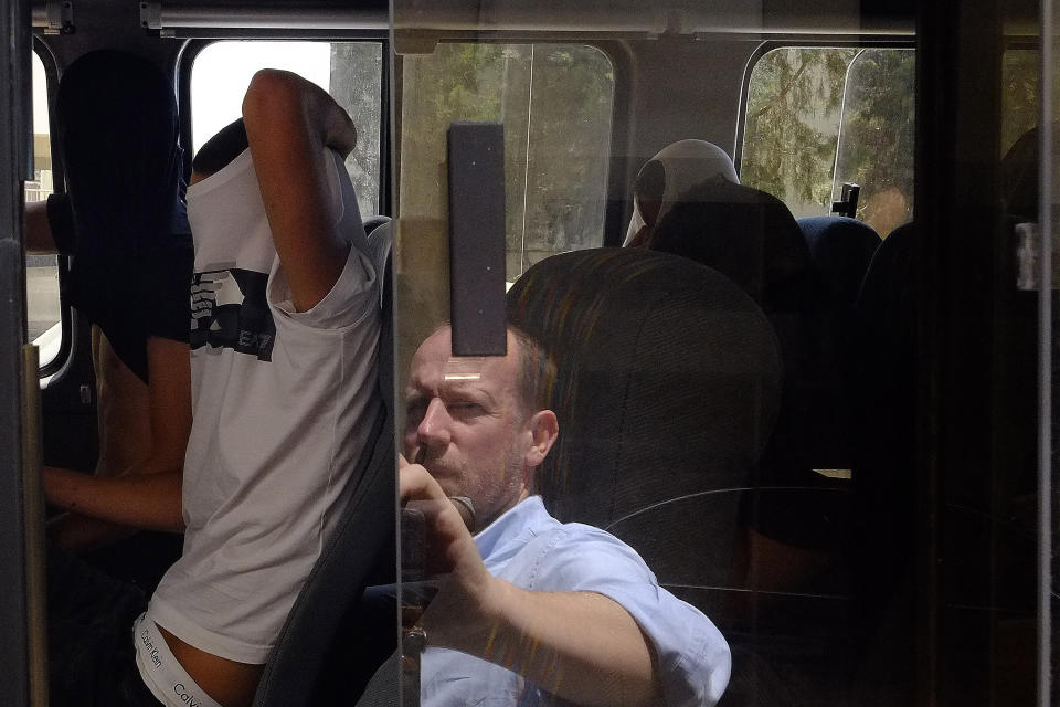 Israeli men cover their faces with their shirts as they sit inside a police vehicle to take them to a detention center outside the Famagusta courthouse in Paralamni, Cyprus on Thursday, July 18, 2019. A Cyprus court has ordered 12 Israelis vacationing on the east Mediterranean island nation to remain in police custody for eight days after a 19-year-old British woman alleged that she was raped. (AP Photo/Petros Karadjias)