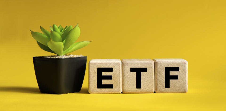 ETF - business financial concept on a yellow background. Wooden cubes and flower in a pot.