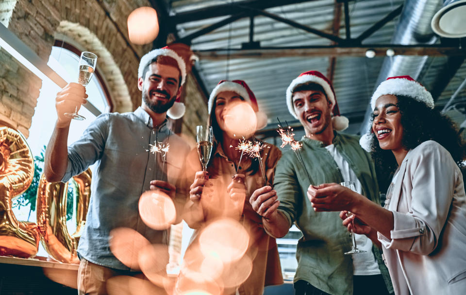 Merry Christmas and Happy New Year 2020!Multiracial young creative people are celebrating holiday in modern office. Group of young business people are drinking champagne with sparkling bengal lights in coworking. Successful hipster team of freelancers.