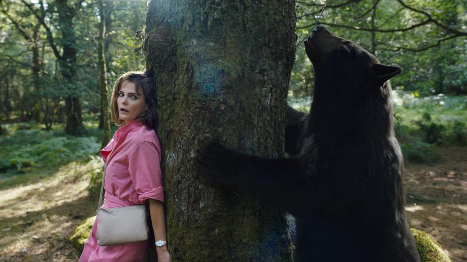 Keri Russell on one side of a tree with a bear on another