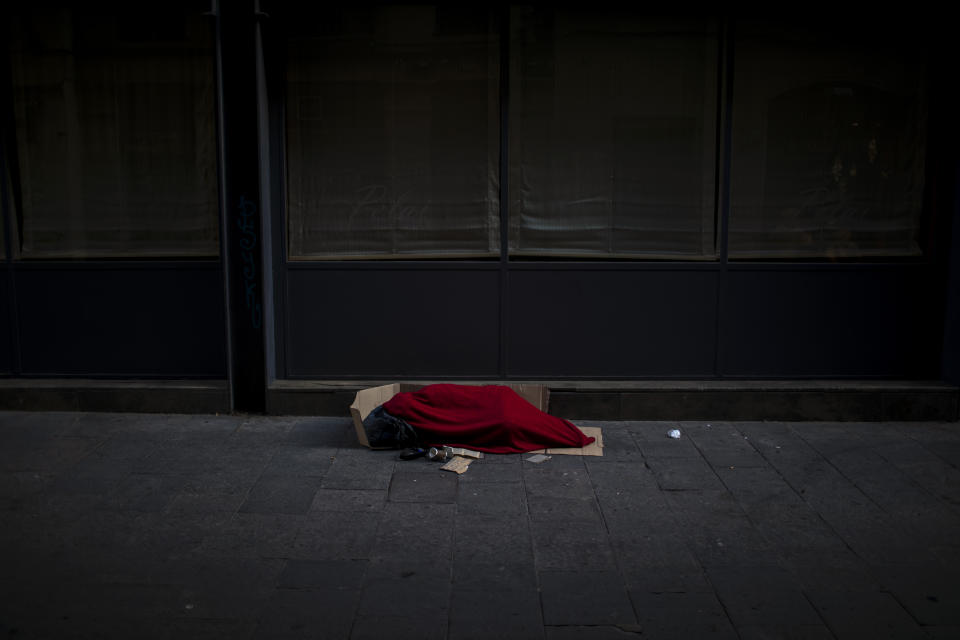 In this Sunday, March 22, 2020 photo, a man covered with a blanket sleeps in an empty street in Barcelona, Spain. In Barcelona sleeping figures with boxes and blankets punctuate the mostly empty city. They are Barcelona's homeless, and there are about 1,000 of them. (AP Photo/Emilio Morenatti)