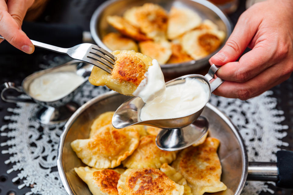 Person serving sour cream on fried ravioli with spoon and fork