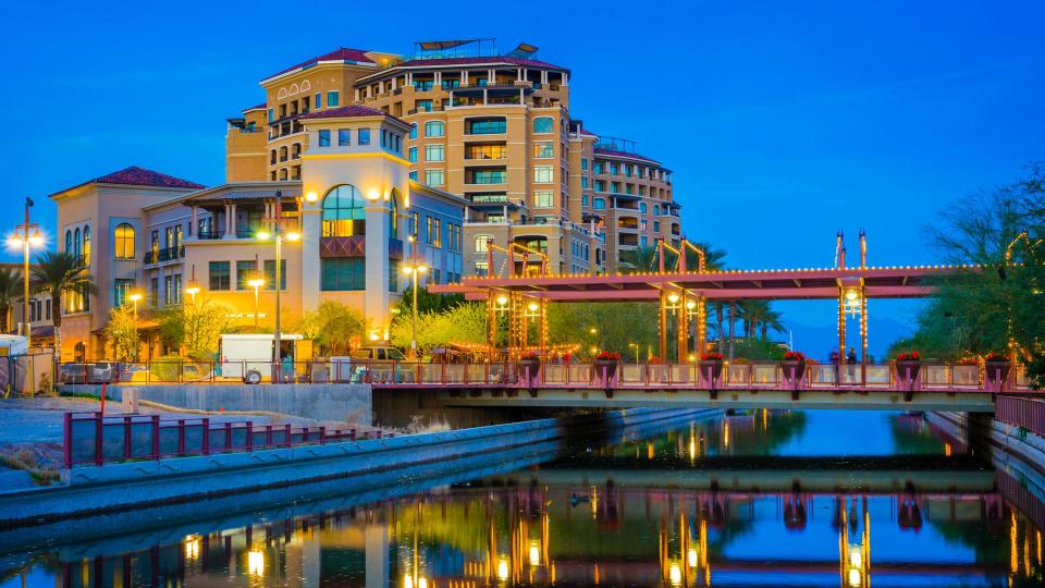 A scene from Downtown Scottsdale at dusk with a canal and reflections in the foreground.