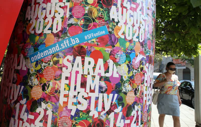 A woman wearing a protective mask walks past the Sarajevo Film Festival posters in Sarajevo