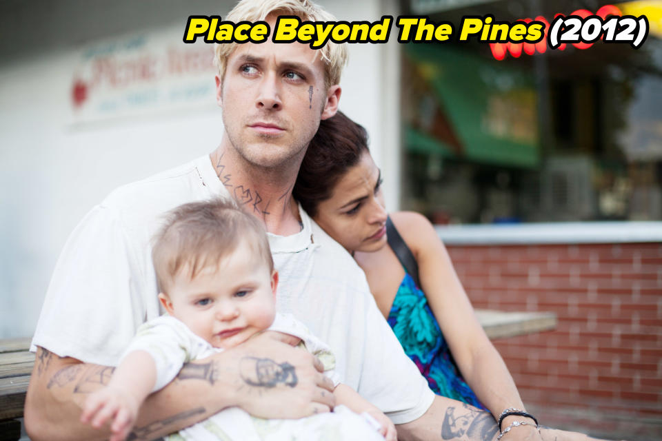 Ryan is sitting and holding a baby as Eva leans on him in a scene from The Place Beyond The Pines