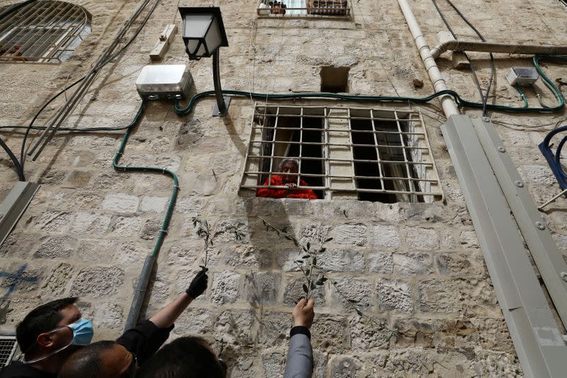 A woman looks down from her window as members of the Latin Patriarchate distribute olive branches to Christian residents on Palm Sunday, during Holy Week amid the coronavirus disease (COVID-19) outbreak, in Jerusalem's Old City