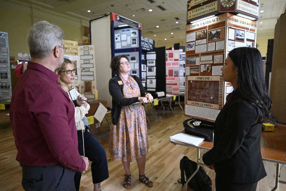 Judges, left to right, John Kutzschebauch, Stacey Trepanned, and Suzanne Jones listen to high school student Jocelyn Hanson, right, of Fresno, Calif., explain her project titled "The Railroad That Changed America: A Turning Point in Transportation", one of the exhibits at the National History Day gathering at the University of Maryland, Tuesday, June 11, 2024, in College Park, Md. (AP Photo/John McDonnell)