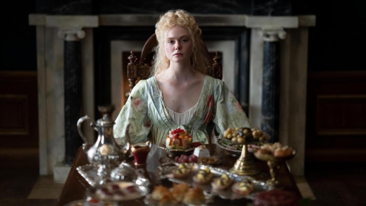  Elle Fanning sitting behind a table looking very sad in The Great. 